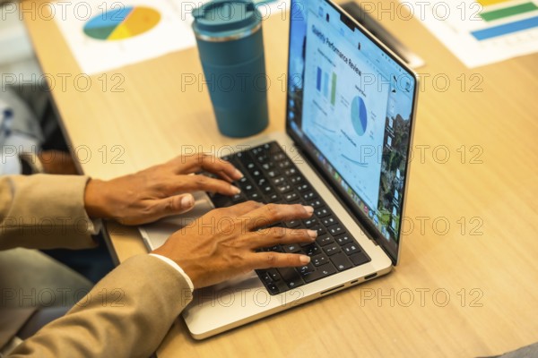Person working on a laptop, hands typing on the keyboard, with a monthly performance review screen showing charts and graphs, indicating data analysis and business operations