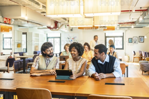 Diverse business colleagues collaborating around a tablet in a modern open plan office, brainstorming ideas, sharing plans and smiling during a productive daytime meeting
