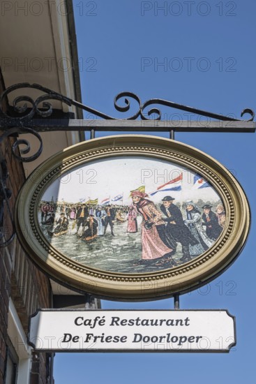 Sign of a café with traditional Dutch illustration in colorful traditional costume under a blue sky, Friesland province, the Netherlands