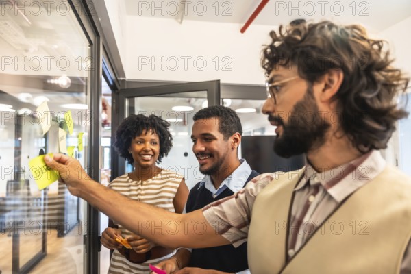 Diverse business colleagues collaborating and developing strategies, sticking colorful notes with ideas onto a glass wall during an office brainstorming session
