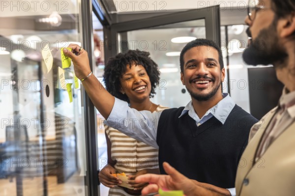 Diverse business professionals collaborating in a modern office, cheerfully sharing innovative ideas during a meeting, placing colorful sticky notes on a glass board
