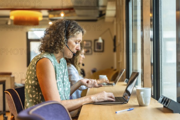 Women concentrating on their work using laptops and headsets in a modern coworking office, demonstrating remote teamwork and professional communication