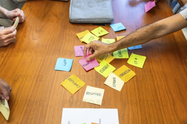 Business team gathered around wooden table arranging colorful sticky notes labeled planning. Marketing. Energy and efficiency. Collaborating on strategy. Creativity and problem solving during meeting