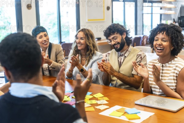 Diverse business colleagues celebrating successful ideas and achievements, clapping and smiling while participating in a collaborative meeting with sticky notes on the table