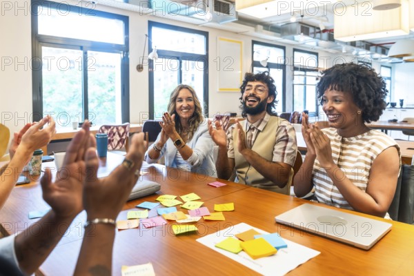 Diverse business colleagues at a modern coworking space collaborating and expressing happiness and appreciation by clapping their hands during a successful workshop