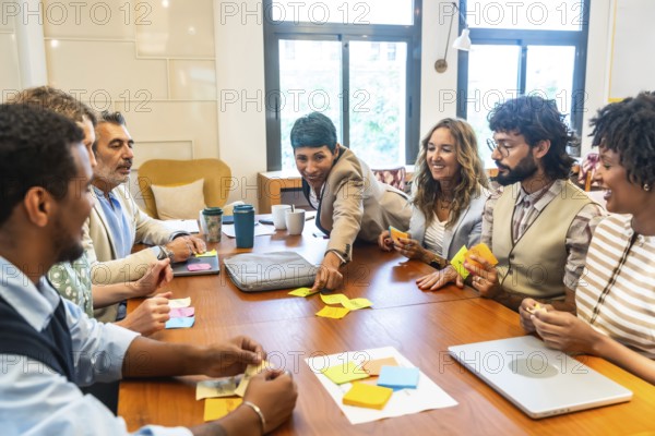Diverse business team collaborating energetically around a table, exchanging ideas, brainstorming with sticky notes and laptops in a modern office to solve problems and plan strategy