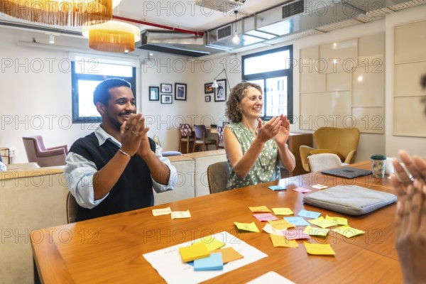 Diverse colleagues participating in a successful meeting, collaborating and brainstorming ideas using sticky notes, and applauding achievements in a modern coworking office