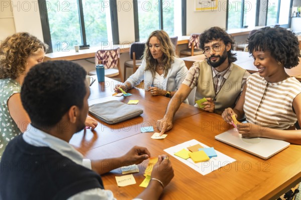 Diverse business team collaborating around a wooden conference table, brainstorming with colorful sticky notes in a modern coworking space during an agile planning session