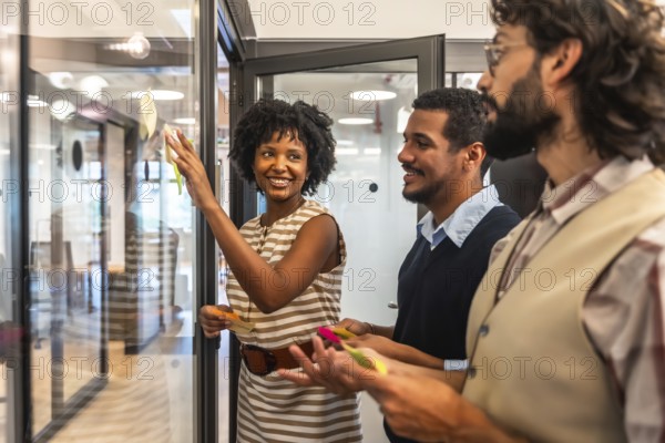 Diverse business professionals collaborating in a modern office, developing new strategies and solutions by placing colorful sticky notes on a transparent partition during a productive meeting