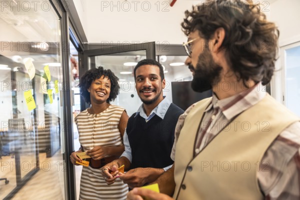 Diverse business professionals collaborating happily, exchanging creative ideas, and planning effectively during an engaging team meeting with sticky notes on a glass wall in an modern office
