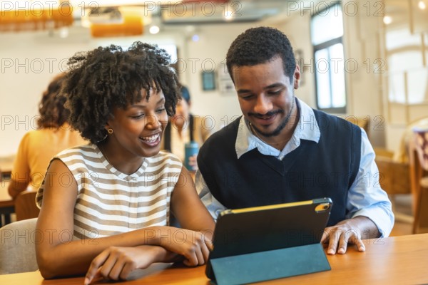 Diverse young business colleagues are enjoying a teamwork moment, looking at a digital tablet together and discussing content in a modern coworking office environment