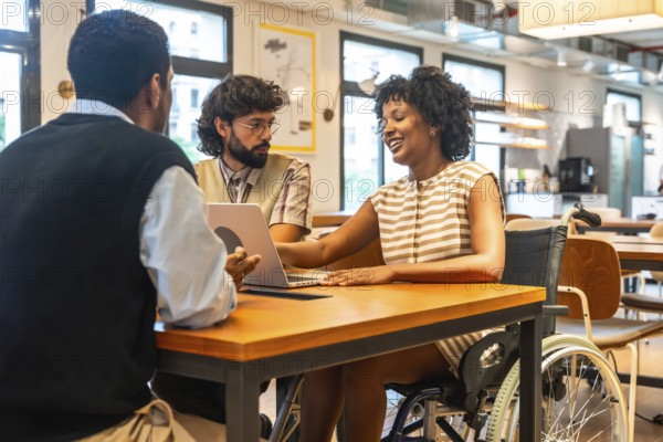 Diverse colleagues collaborating around a modern coworking table, smiling and brainstorming with a laptop, inclusive team includes a woman in a wheelchair, promoting accessibility and teamwork