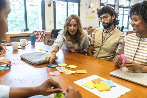 Diverse team of professionals collaborating, strategizing, and sharing concepts using colorful sticky notes on a wooden table in a modern office or coworking space