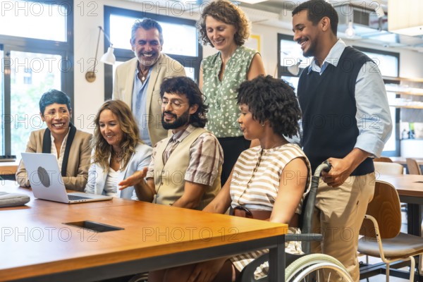 Diverse corporate team smiling and collaborating around a laptop in an inclusive coworking office, featuring colleagues with various backgrounds and abilities working together productively