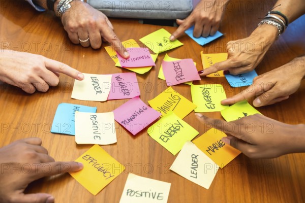 Business colleagues gathered around a wooden table point at colorful sticky notes labeled planning, leadership, energy and efficiency, illustrating teamwork, brainstorming and project strategy