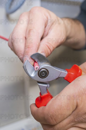 Electrician uses pliers to cut red wire close-up