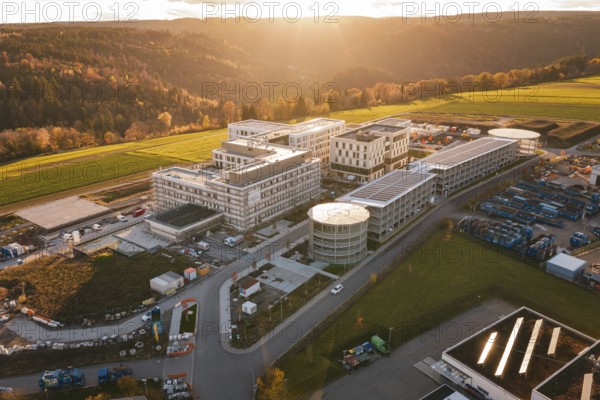 Modern buildings surrounded by fields and hills at sunset, aerial view, new hospital, Calw health campus, Black Forest, Germany