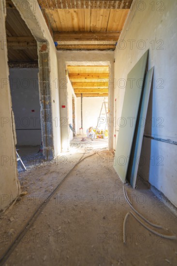 A shell with sunlight in the corridor. Cables, unfinished walls and a wooden floor define the room