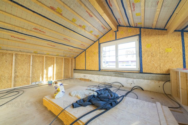 Unfinished construction of an attic with insulation on the walls. Large windows let in lots of light