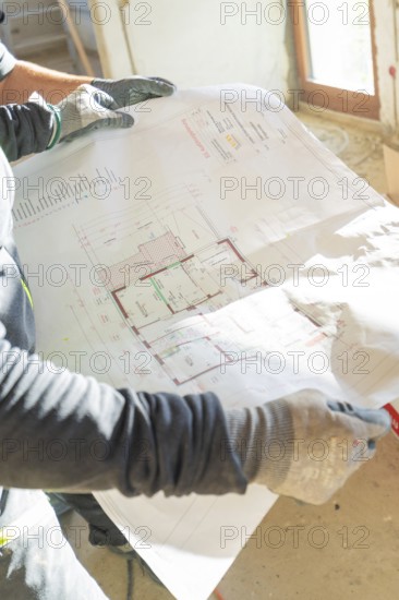 A construction worker holds a construction plan in his hands in a light-filled room