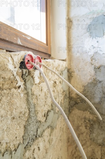 Cables stick out of an unfinished wall near a window during renovations