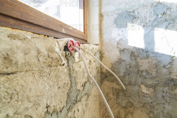 Cables hang loose from an unfinished wall, next to windows during renovation
