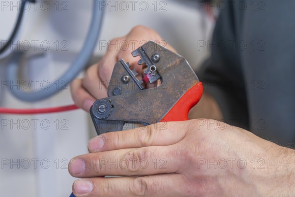 Hand holding pliers that process a cable, industrial environment