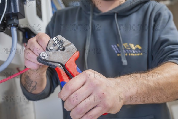 Electrician uses pliers to cut off a red cable, focus on tools