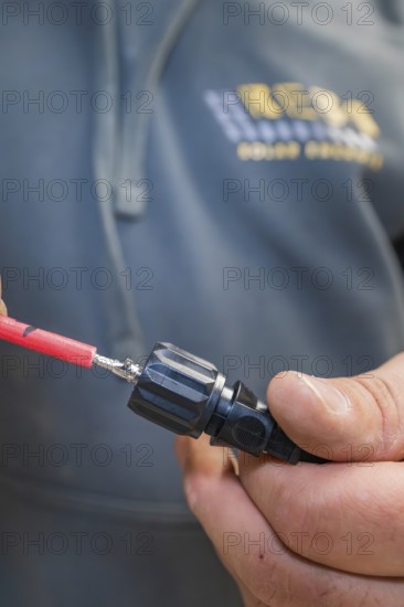 Electrician sitting with cable plug in hand, focus on connecting cable