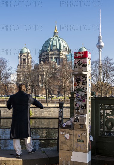 A man stands next to a demolished modern Telekom telephone column, view of Lustgarten Cathedral, Berlin, Germany