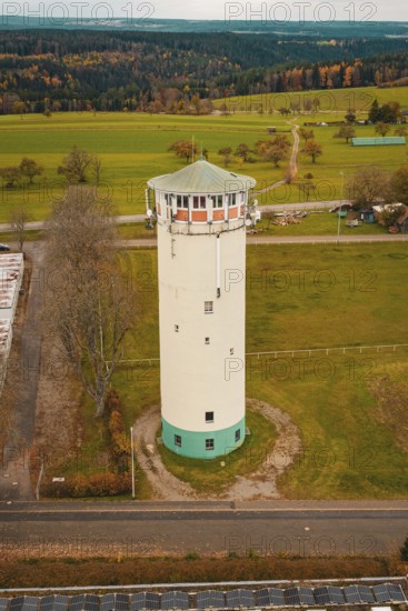 White water tower in rural autumn landscape with green fields and autumnal trees, water tower, Pfalzgrafenweiler, Freudenstadt district, Germany