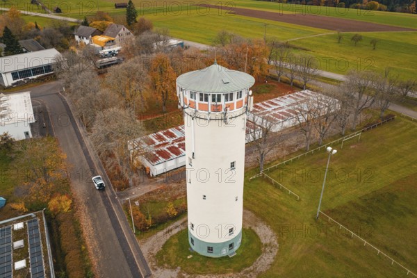 Water tower on a road with autumn trees in rural area, surrounded by small buildings, water tower, Pfalzgrafenweiler, Freudenstadt district, Germany