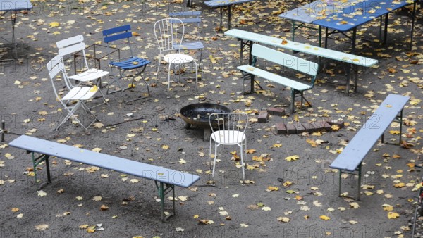 Chairs and tables stand unsorted around a fire bowl, a celebration in the garden is over, colorful autumn leaves everywhere, Berlin, Germany