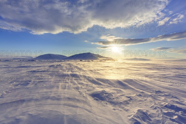 Midnight sun over windswept snow covered Arctic landscape at Mohnbukta, bay at western shore of Storfjorden in Sabine Land, Spitsbergen, Svalbard
