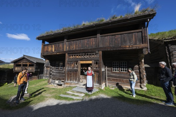 Tourist guide in traditional traditional costume and visitor, Bjørnstad, farm from Vågå, Maihaugen open-air museum with houses and objects from farms in Gudbrandsdal, Lillehammer am Mjøsa Lake, Fylke Innlandet Municipality, Norway