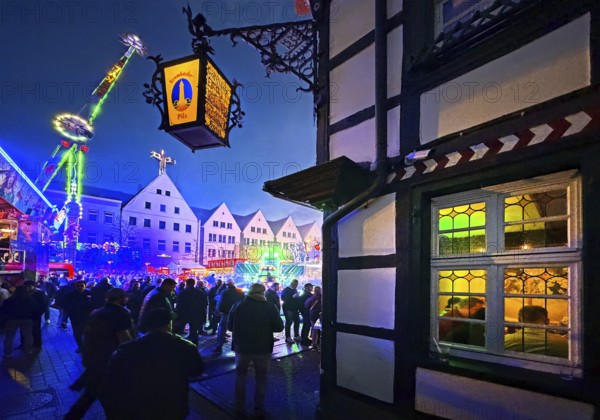 All Saints Fair in the evening with a half-timbered house and colorful illuminated rides, Old Town, Soest, North Rhine-Westphalia, Germany