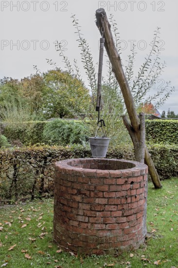 An old brick well with a bucket in an autumnal garden, Münsterland, North Rhine-Westphalia, Germany