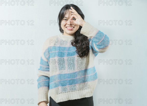 Beautiful asian woman making OK gesture looking through fingers isolated. Smiling asian girl making gesturing OK looking through fingers