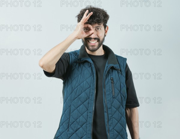 Cheerful guy making ok gesture looking through fingers. Handsome young man making OK gesture looking through fingers isolated