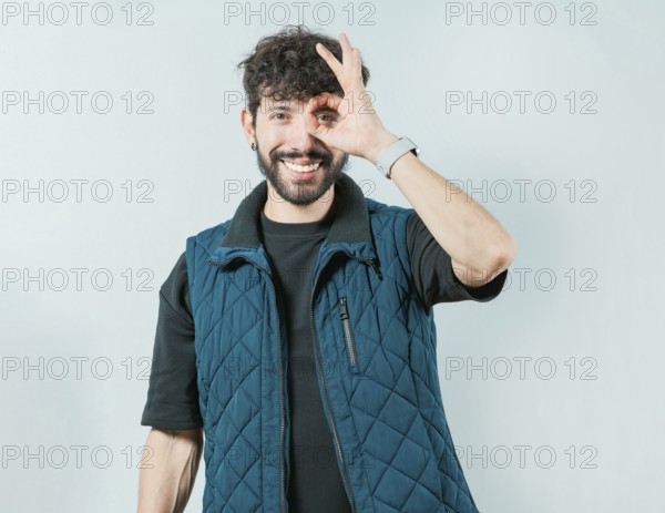 Handsome young man making OK gesture looking through fingers isolated. Cheerful guy making ok gesture looking through fingers