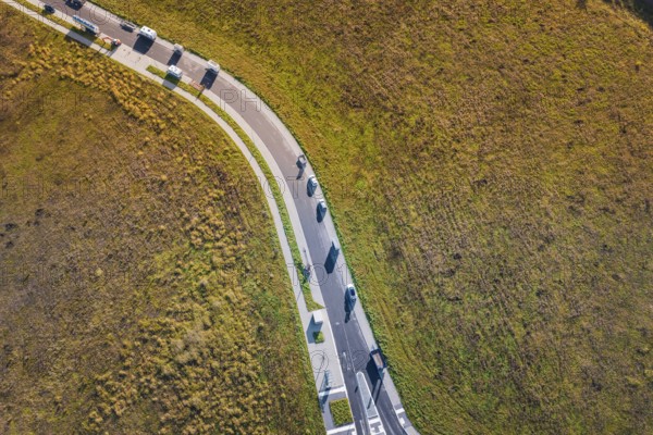 Curved road with cars through autumnal meadow landscape, new Lindenrain industrial park, Calw, Black Forest, Germany