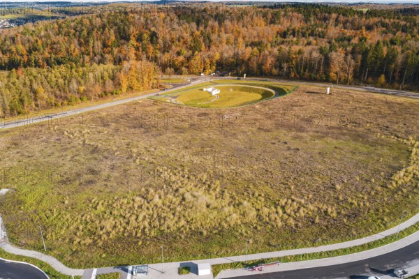 Wide meadow area surrounded by autumn-colored forest and roads, new Lindenrain industrial park, Calw, Black Forest, Germany
