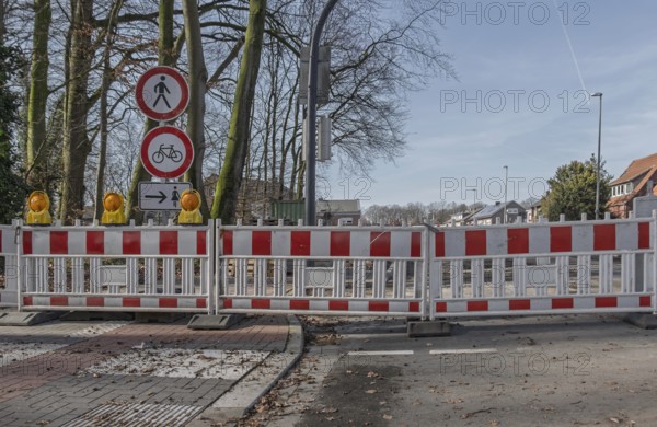 Road block with warning signs and yellow lights surrounded by bare trees in winter, Münsterland, North Rhine-Westphalia, Germany