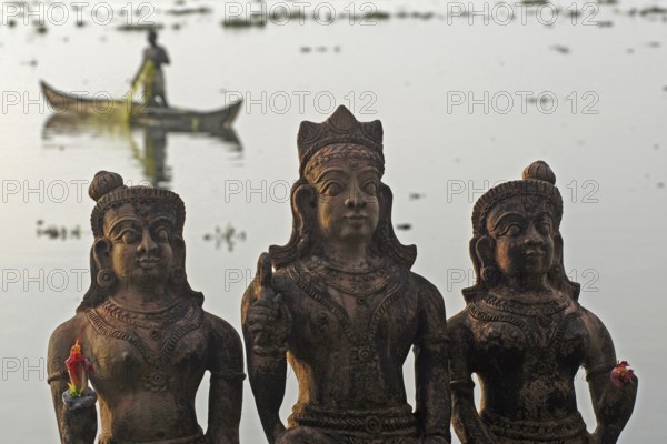 Three Hindu god statues made of clay, fishermen in a boat in the background, Vembanad Lake, Kerala, India