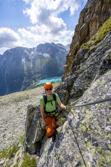 Mountaineer climbs on steep rock face in the secured via ferrata Crocodile Mountain Lake at Bergseeschijen-Vorbau, Göscheneralp, Canton of Uri, Switzerland