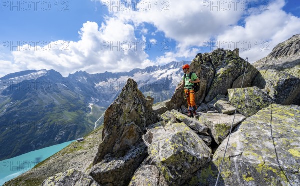 Mountaineers between boulders on the secured via ferrata Crocodile Mountain Lake at Bergseeschijen-Vorbau, view of dam glacier and dammastock, Göscheneralp, Canton of Uri, Switzerland