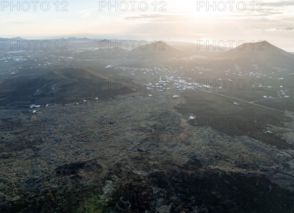 Picturesque volcanic landscape with volcanic craters and lava fields in the morning light, white houses in the village of Masdache, Parque Natural de Los Volcanes, aerial view, Lanzarote, Canary Islands, Spain