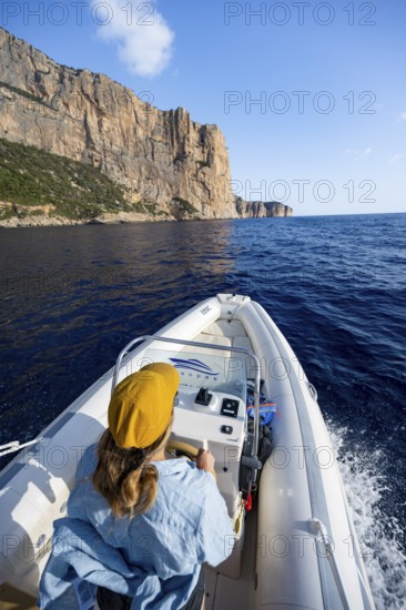 Young woman riding a motor boat along the picturesque rocky coast, cliffs and blue sea, Golfo di Orosei, Baunei, Sardinia, Italy