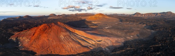 Picturesque volcanic landscape in evening light, red volcano Montaña Bermeja between lava fields, aerial view, Lanzarote, Canary Islands, Spain