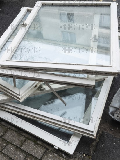 A pile of old white window frames with glass is lying on a sidewalk in Wuppertal, Germany